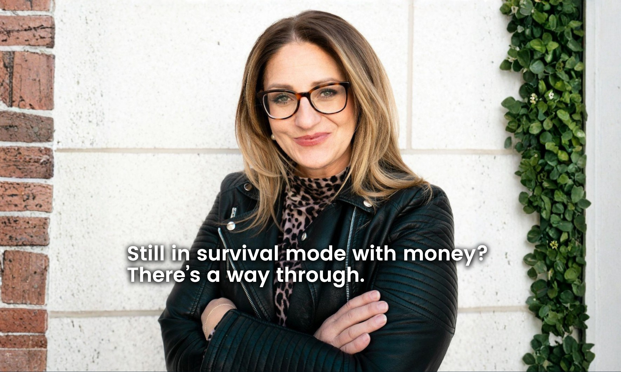 Alison-Pickett-True-Path-Founder-Money-Mindset Meet Alison Pickett. This photo is a picture of Alison, a middle aged C-Suite business woman with a kind smile, beautiful shoulder-length dirty blonde hair, glasses, and pearl earrings. She has her arms folded, and is wearing a cool black leather jacket and cheeta print scarf. The overlaying text reads "Still in survival mode with money? There's a way through."